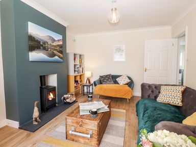 A living room with a wood burning stove paintings sofas and a wooden coffee table at Pooley Howe in Keswick