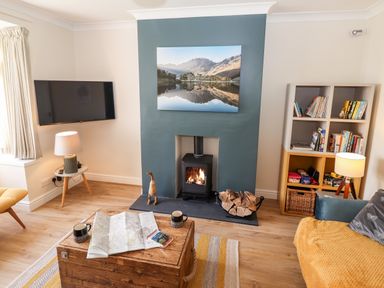 A living room with a fireplace wood stove a TV mounted on the wall a wooden chest a bookshelf and a sofa at Pooley Howe in Keswick