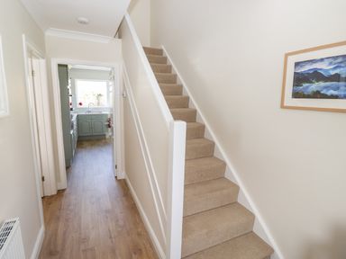 A hallway with carpeted stairs on the right and a kitchen visible at the end at Pooley Howe in Keswick