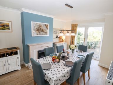 A dining room with a table covered with a tablecloth and six chairs and a blue accent wall with a fireplace at Pooley Howe in Keswick