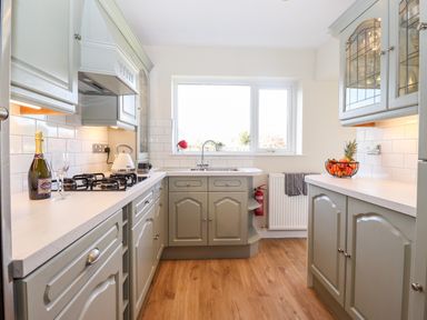 A kitchen with green cabinets white countertops a window over the sink and a fruit basket on the counter at Pooley Howe in Keswick