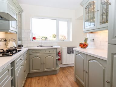 A kitchen with green cabinets white countertops a window a stove a kettle and a fruit bowl at Pooley Howe in Keswick