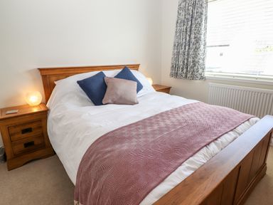 A bedroom with a wooden bed, white bedding, blue and beige pillows, bedside tables with lamps and a window with patterned curtains at Pooley Howe in Keswick