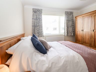 A bedroom with a wooden bed and wardrobe with curtains on the window at Pooley Howe in Keswick
