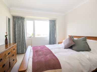 A bedroom with a wooden bed and dresser a mirror window with curtains at Pooley Howe in Keswick