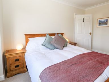 A bedroom with a wooden bed frame white bedding red throw pillows wooden nightstands with lamps and a door at Pooley Howe in Keswick
