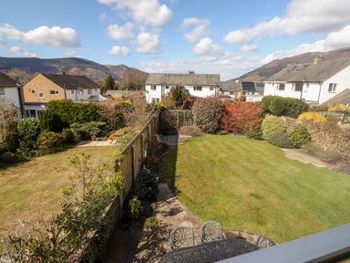 A backyard with green grass patios bushes and houses in the background at Pooley Howe in Keswick