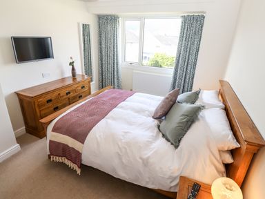 A bedroom with a wooden bed and dresser a wall mounted TV and a window at Pooley Howe in Keswick