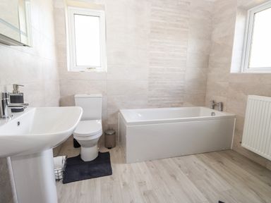 A bathroom with a sink, toilet, bathtub, two windows, a radiator, and a small trash can at Pooley Howe in Keswick