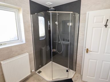 A bathroom with a corner glass shower enclosure a white window a white door and a white radiator at Pooley Howe in Keswick