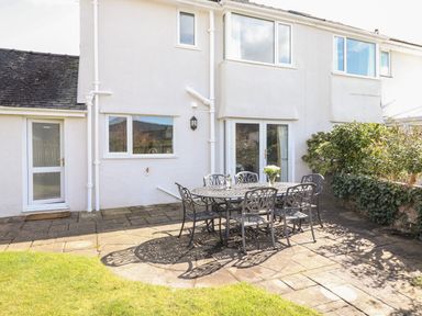 An outdoor patio with a metal table and six chairs beside a white house with windows and doors at Pooley Howe in Keswick