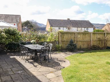 A backyard with a metal table and chairs on a stone patio and a wooden fence at Pooley Howe in Keswick
