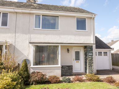 A two story house with white exterior walls a front door and large window with vertical blinds at Pooley Howe in Keswick