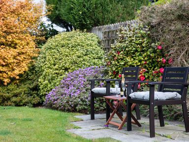 A garden area with two chairs and a small table with a bottle and glasses surrounded by various bushes and flowers at Pooley Howe in Keswick
