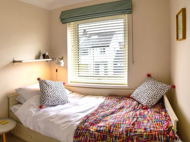 A bedroom with a single bed featuring white bedding, two spotted pillows, a colorful blanket, a window with blinds, a wall lamp, and a small round side table at Pooley Howe Keswick
