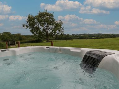 A hot tub with bubbling water outdoors overlooking a green field and a tree at Swallows Nest in Puxey near Sturminster Newton