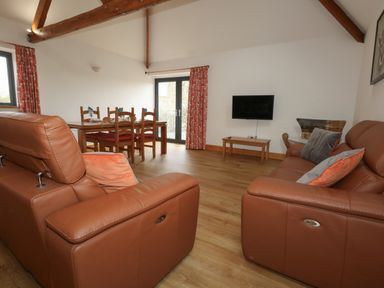 A living room with brown leather sofas a wooden dining table with chairs a wall-mounted TV and wooden beams at Swallows Nest in Puxey near Sturminster Newton