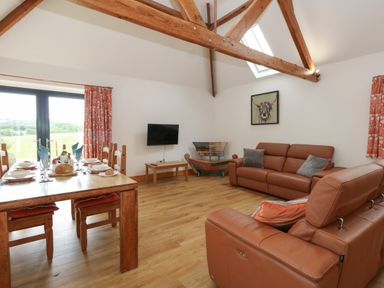 A living room with leather sofas a wooden dining table set for a meal a wall mounted tv and exposed wooden ceiling beams at Swallows Nest in Puxey near Sturminster Newton