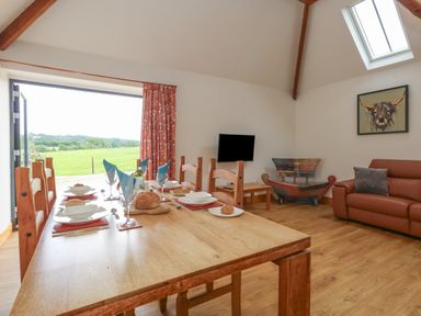 A dining room with wooden table and chairs set for meal next to a sitting area with sofa and TV at Swallows Nest in Puxey near Sturminster Newton