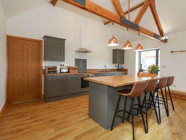 A kitchen with wooden floor grey cabinets an island with four brown bar stools and wooden beams at Swallows Nest in Puxey near Sturminster Newton
