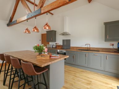 A kitchen with wooden countertops gray cabinets brown bar stools and copper pendant lights at Swallows Nest in Puxey near Sturminster Newton