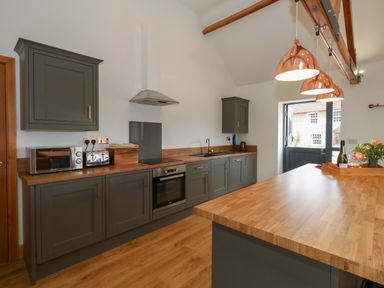 A kitchen with grey cabinets wooden countertops pendant lights and a door at Swallows Nest in Puxey near Sturminster Newton