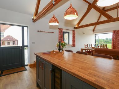 A kitchen island with wooden countertop and hanging copper pendant lights in an open plan room at Swallows Nest in Puxey near Sturminster Newton