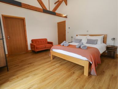 A bedroom with a wooden bed with white and gray bedding two wooden doors and an orange sofa at Swallows Nest in Puxey near Sturminster Newton