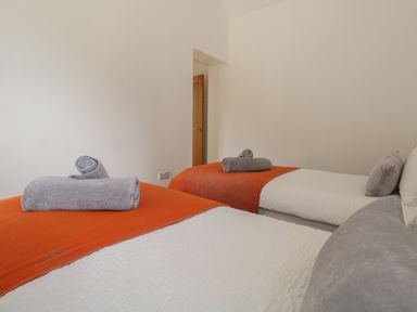 A bedroom with two single beds covered with white quilts and orange throws with gray towels on top at Swallows Nest in Puxey near Sturminster Newton