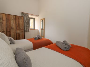 A bedroom with two single beds with orange throws and gray towels and pillows and a wooden wardrobe at Swallows Nest in Puxey near Sturminster Newton