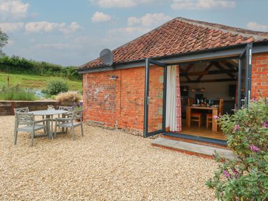 An outdoor patio with a round table and four chairs next to a brick house with open doors revealing a dining area at Swallows Nest in Puxey near Sturminster Newton