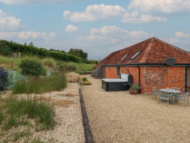 A gravel patio with a hot tub and outdoor dining set next to a brick building with a tiled roof at Swallows Nest in Puxey near Sturminster Newton