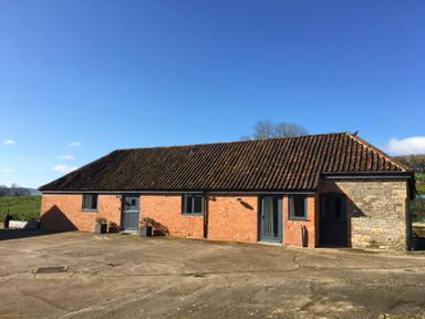 A single-story brick building with a tiled roof and multiple doors and windows at Swallows Nest in Puxey near Sturminster Newton