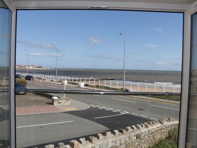 A view of a road and beach with railings and street lamps seen through a window at Ocean View Apartment in Colwyn Bay