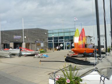A marina area with boats kayaks and a bike hire shop near a building entrance with people sitting outside at Ocean View Apartment in Colwyn Bay