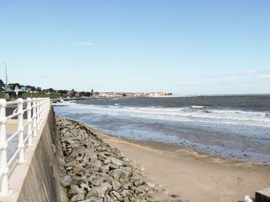 A coastal scene with a seawall railing a rocky shoreline sandy beach and waves at Ocean View Apartment in Colwyn Bay