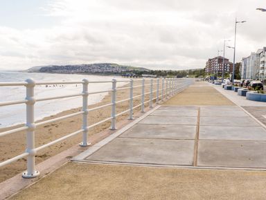 A seaside promenade with railing and sandy beach and buildings in the distance at Ocean View Apartment in Colwyn Bay