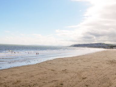 A sandy beach with people in the water and a town on the hillside in the distance at Ocean View Apartment in Colwyn Bay