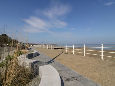 A seafront promenade with curved stone benches and a railing along the beach at Ocean View Apartment in Colwyn Bay