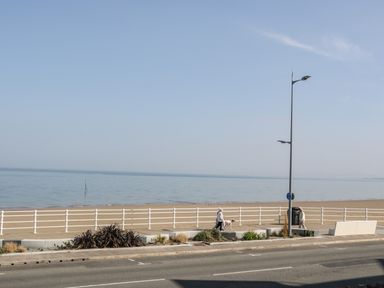 A beach with a railing and a sidewalk with two people walking and a street with a lamppost at Ocean View Apartment in Colwyn Bay