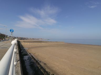 A beach with a sandy shore next to a promenade with railings and a bike and pedestrian sign at Ocean View Apartment in Colwyn Bay
