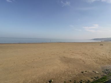 A sandy beach with a calm sea and a few people walking in the distance at Ocean View Apartment in Colwyn Bay