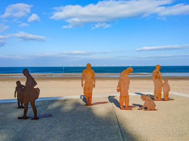 Metal sculptures of people on a paved area near a beach with the sea and wind turbines in the background at Ocean View Apartment in Colwyn Bay