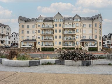 A large apartment building with balconies and multiple windows behind a road and concrete planter at Ocean View Apartment in Colwyn Bay