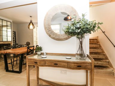 A wooden console table with drawers and a glass vase with foliage next to stairs and a round mirror above at 23 Daniel Street in Bath