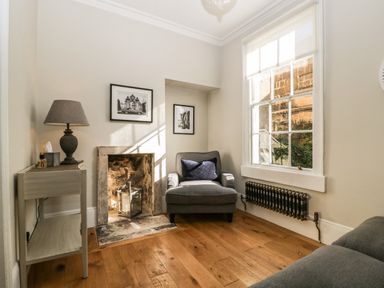 A sitting room with a gray armchair near a fireplace and a window at 23 Daniel Street in Bath