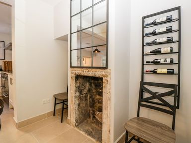 A corner with an old fireplace a large mirror above it two wooden chairs and a vertical wine rack with bottles at 23 Daniel Street in Bath
