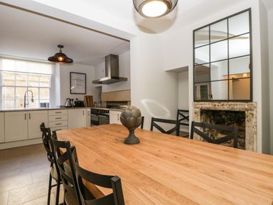 A dining area with a wooden table and black chairs next to a kitchen with white cabinets and a stainless steel range at 23 Daniel Street in Bath