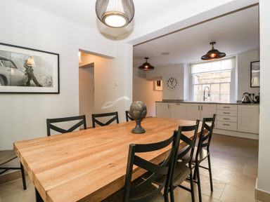 A dining area with a wooden table and black chairs connected to a kitchen with white cabinets and a window at 23 Daniel Street in Bath