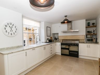 A kitchen with white cabinets granite countertops a large window a clock on the wall and a stove at 23 Daniel Street in Bath